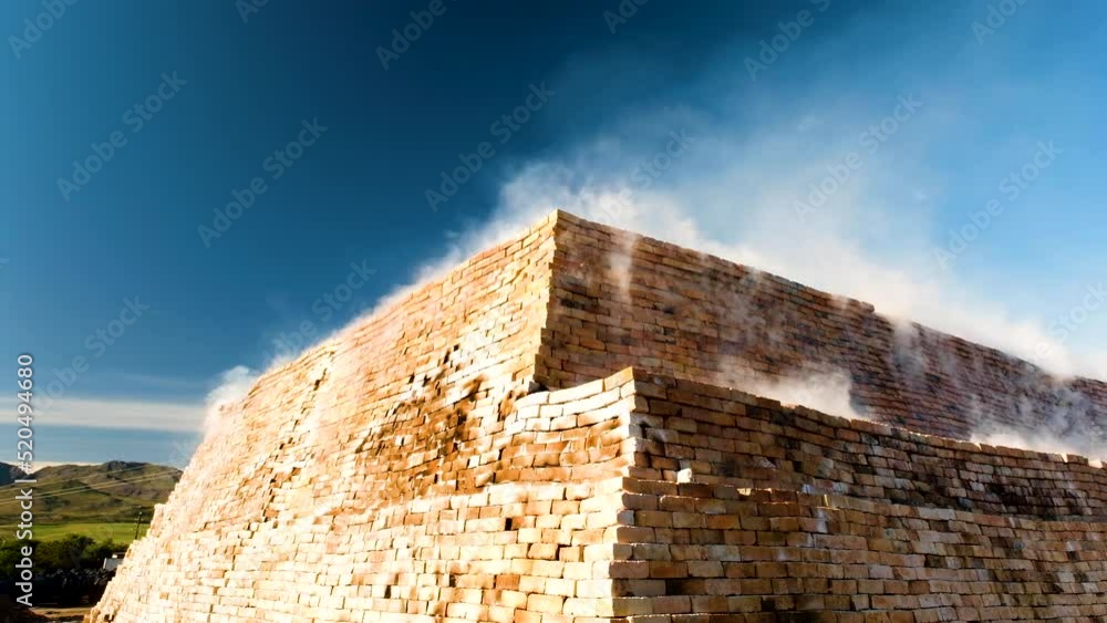 Clay bricks being fired in clamp kiln with smoke rising from the heap