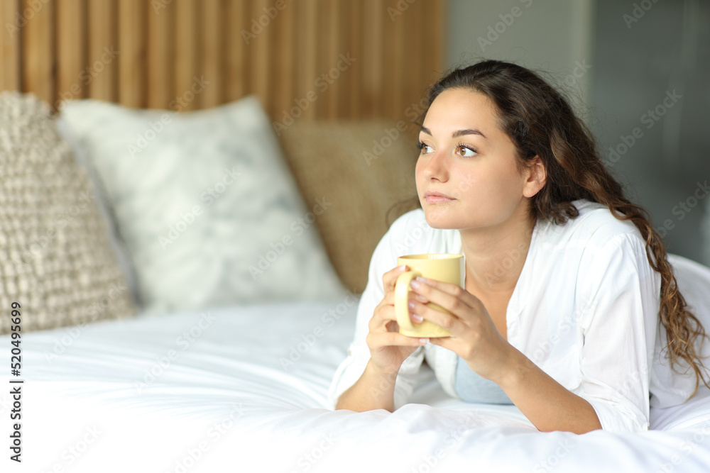 Distracted woman looking away drinking coffee on a bed Distracted woman looking away drinking coffee on a bed