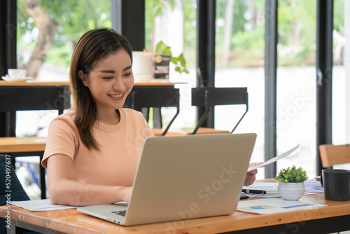 Beautiful smiling Asian businesswoman sitting at a desk and using a laptop in an office.
