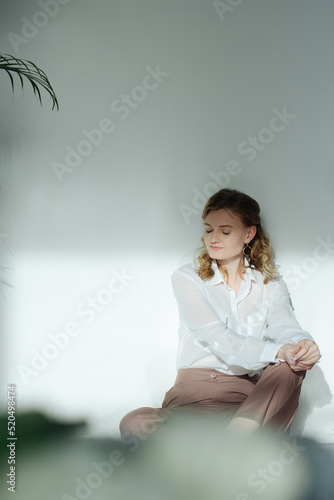 a woman relaxes against the wall covering her eyes in a white blouse. sitting on the floor and completely immersed in the inner feelings of yourself