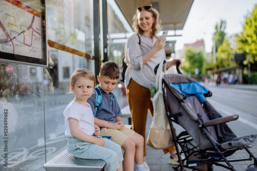 Young mother with little kids waiting on bus stop in city. Young mother with little kids waiting on bus stop in city.