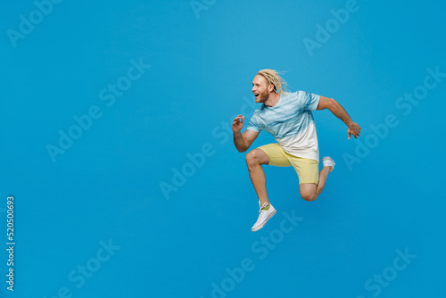 Full body side view sporty happy young blond man with dreadlocks 20s he wear white t-shirt jump high run fast isolated on plain pastel light blue background studio portrait. People lifestyle concept