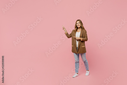 фотографія Full body young successful employee business woman 30s she wear casual brown classic jacket point index finger aside on workspace area mock up isolated on plain pastel light pink background studio