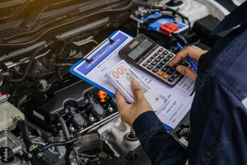 Hands of machinic man holding calculator and money, dollar banknotes to charge service and writing to the clipboard the checklist for repair machine, car service and maintenance.