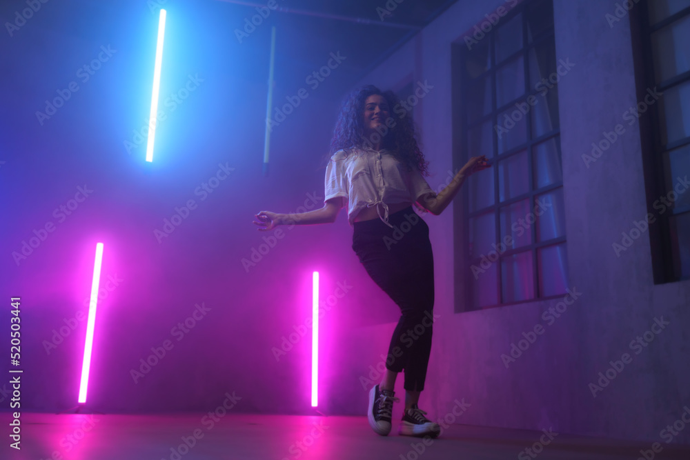 Portrait of a happy young woman dancing over neon light background at disco party