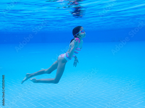 Brave girl with goggles diving in the blue waters of a swimming pool. Sport, recreation, lifestyle concept