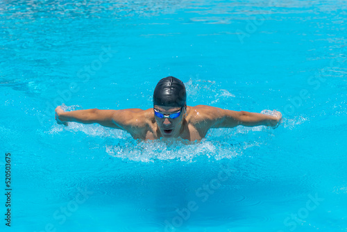 Close up action shot of athlete, young man, teenager swimming butterfly style. Sport, recreation concept.