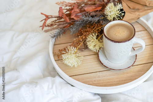 Cup of coffee cappuccino in bed on a white sheet of bedding linen with flowers. Cozy warm morning concept