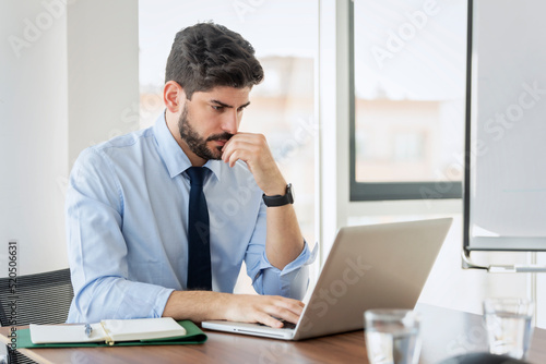 Confident businessman using laptop while sitting at office desk and working