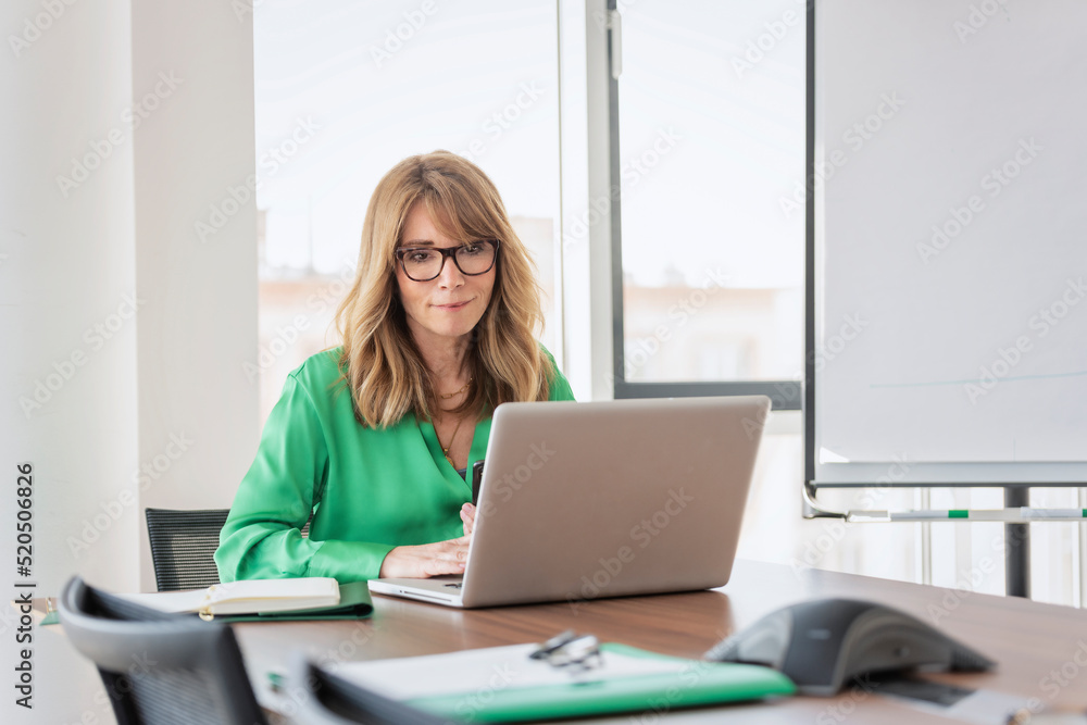 Confident middle aged businesswoman using laptop while working at the office Confident middle aged businesswoman using laptop while working at the office