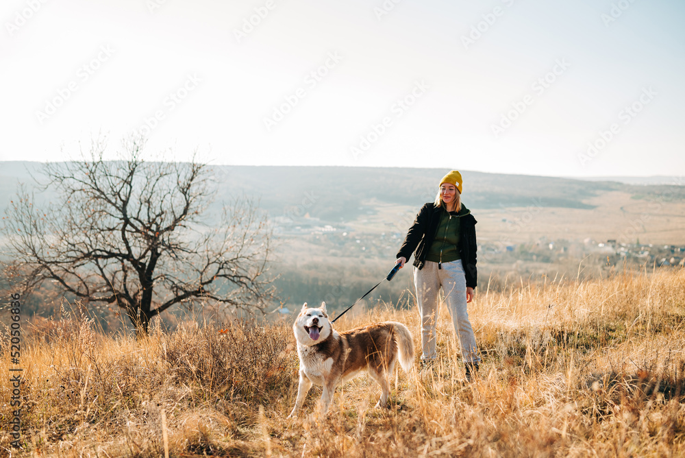 Young woman and her husky dog trek down a forest trail offering a scenic view of the trees changing colors. Fit girl takes her miniature pinscher for a walk in woods