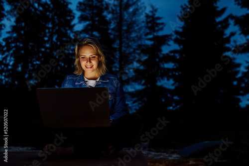 Woman, freelancer working on laptop, sitting outdoor in the evening, concept of remote office, work during vacation.