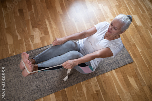 Senior caucasian woman doing abs exercises, sitting in boat yoga pose at home.