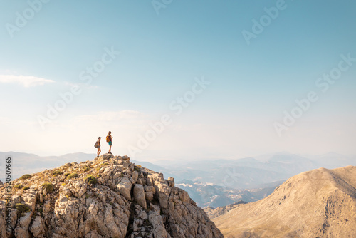two girls with backpacks stand on top of a mountain.