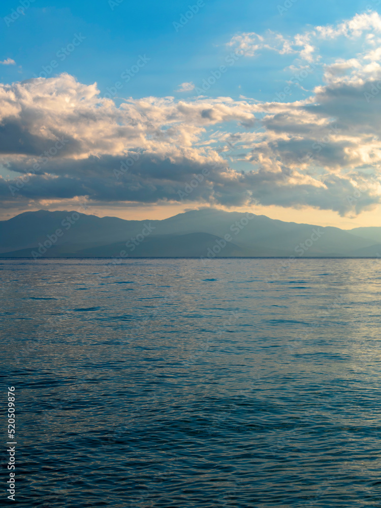 Cloudy sky above the sea and mountains in the horizon's background. The change of weather is continuous in all seasons. Calm and serene, scenic view.