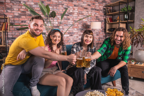 At home in living room group of multiracial friends very charismatic and enthusiastic watch a football match on tv channel they take some snacks and beer