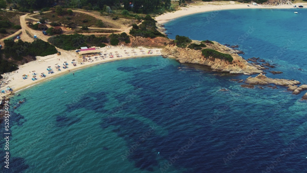 Obraz premium Some tourists relaxing on quiet sandy beach of Sarti. Greek summer holidays. Aerial view. Shallow turquoise sea water. High quality photo