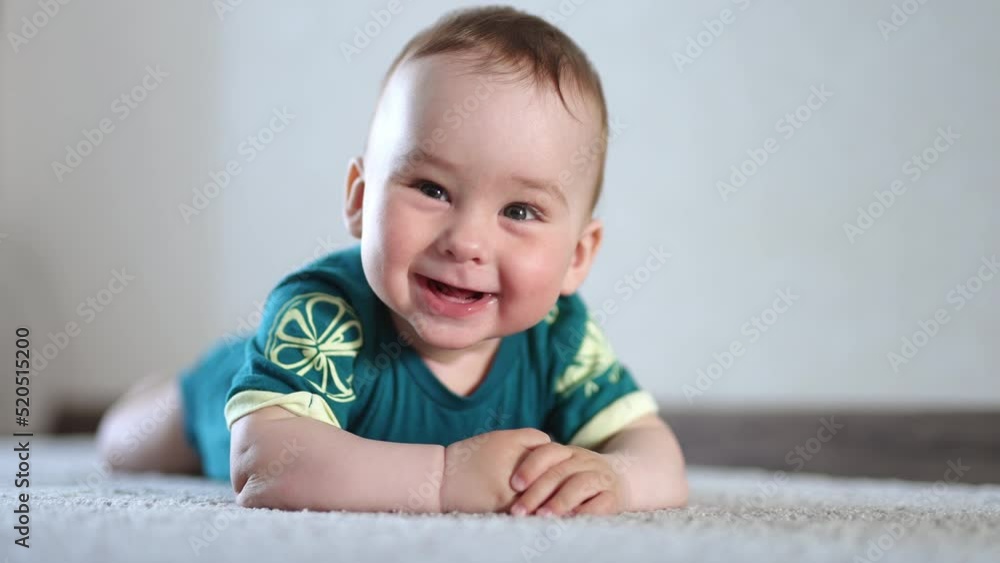 Adorable smiling kid lies on the floor looking at camera. Cheerful kid banging hands by the floor actively. Close up. Adorable smiling kid lies on the floor looking at camera. Cheerful kid banging hands by the floor actively. Close up.