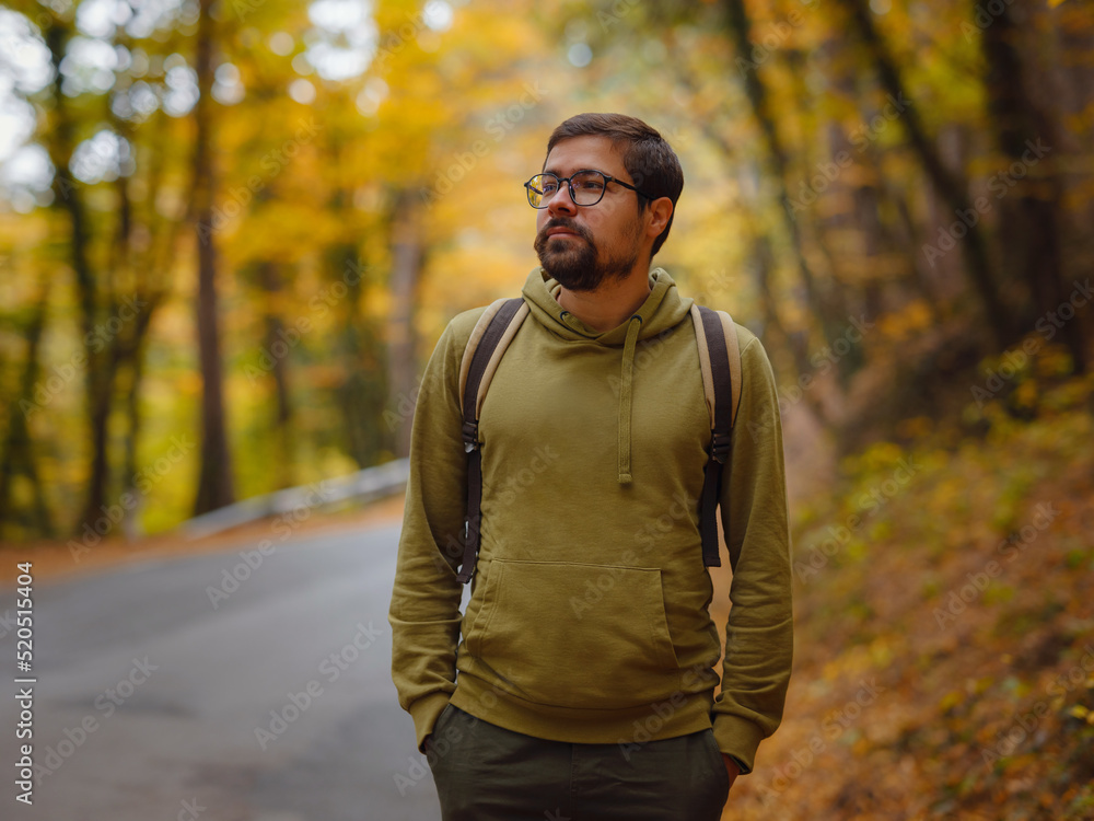 Young handsome man posing in autumn forest on road. young hipster guy with backpack , traveller standing in woods, Hiking, Forest, Journey, active healthy lifestyle, adventure, vacation concept. Young handsome man posing in autumn forest on road. young hipster guy with backpack , traveller standing in woods, Hiking, Forest, Journey, active healthy lifestyle, adventure, vacation concept.