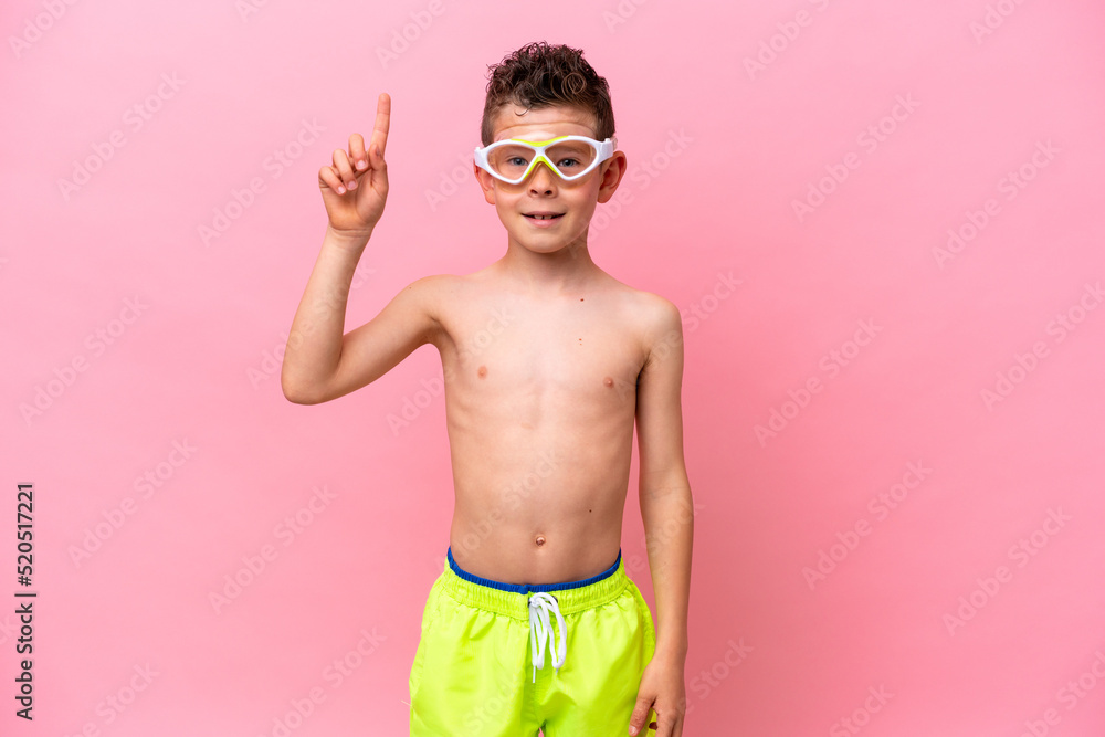 Little caucasian boy wearing a diving goggles isolated on pink background pointing up a great idea