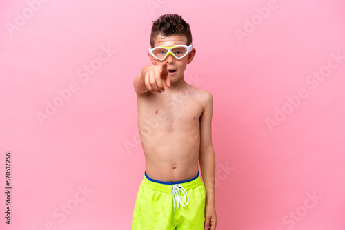 Little caucasian boy wearing a diving goggles isolated on pink background surprised and pointing front