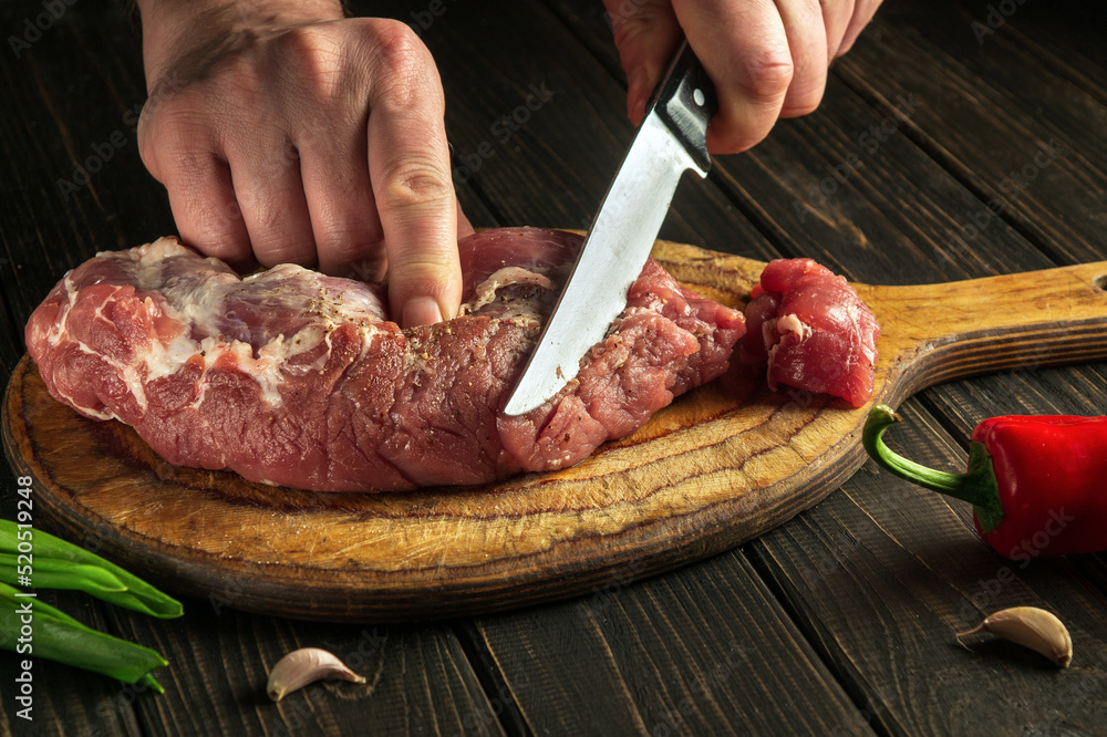 Butcher or chef cuts raw beef meat on a cutting board before baking. Hotel menu recipe idea
