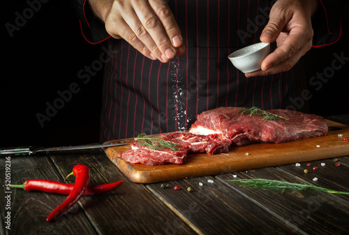 The chef salts raw fresh beef before roasting or grilling. Working environment in the kitchen of a restaurant or hotel.
