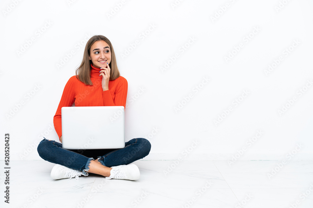 Young caucasian woman sitting on the floor with a laptop thinking an idea while looking up Young caucasian woman sitting on the floor with a laptop thinking an idea while looking up