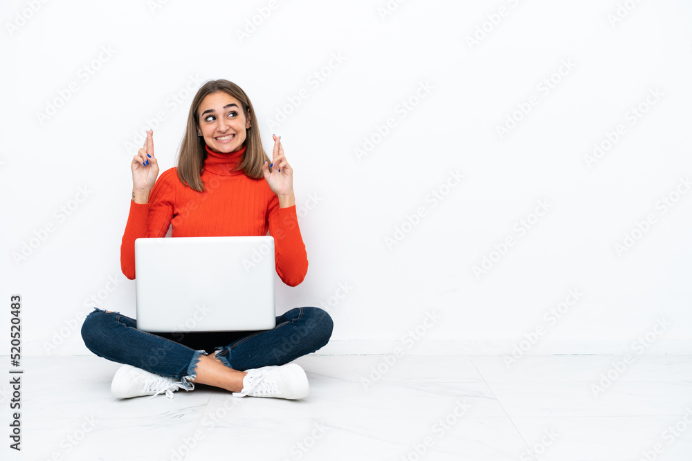 Young caucasian woman sitting on the floor with a laptop with fingers crossing Young caucasian woman sitting on the floor with a laptop with fingers crossing
