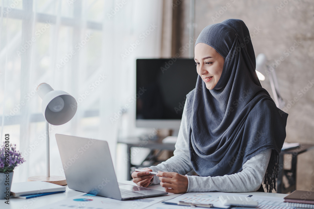 happy muslim business women in hijab at work smiling arab woman taking notes and work on laptop happy muslim business women in hijab at work smiling arab woman taking notes and work on laptop