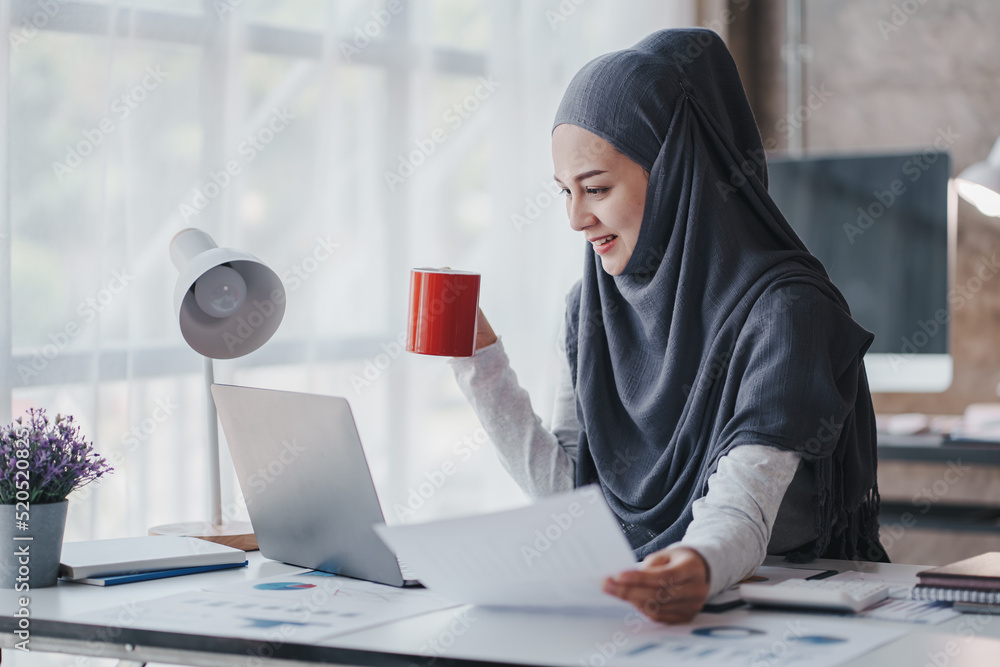 happy muslim business women in hijab at work smiling arab woman taking notes and work on laptop happy muslim business women in hijab at work smiling arab woman taking notes and work on laptop
