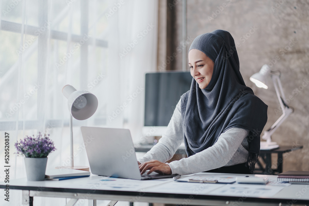 happy muslim business women in hijab at work smiling arab woman taking notes and work on laptop happy muslim business women in hijab at work smiling arab woman taking notes and work on laptop