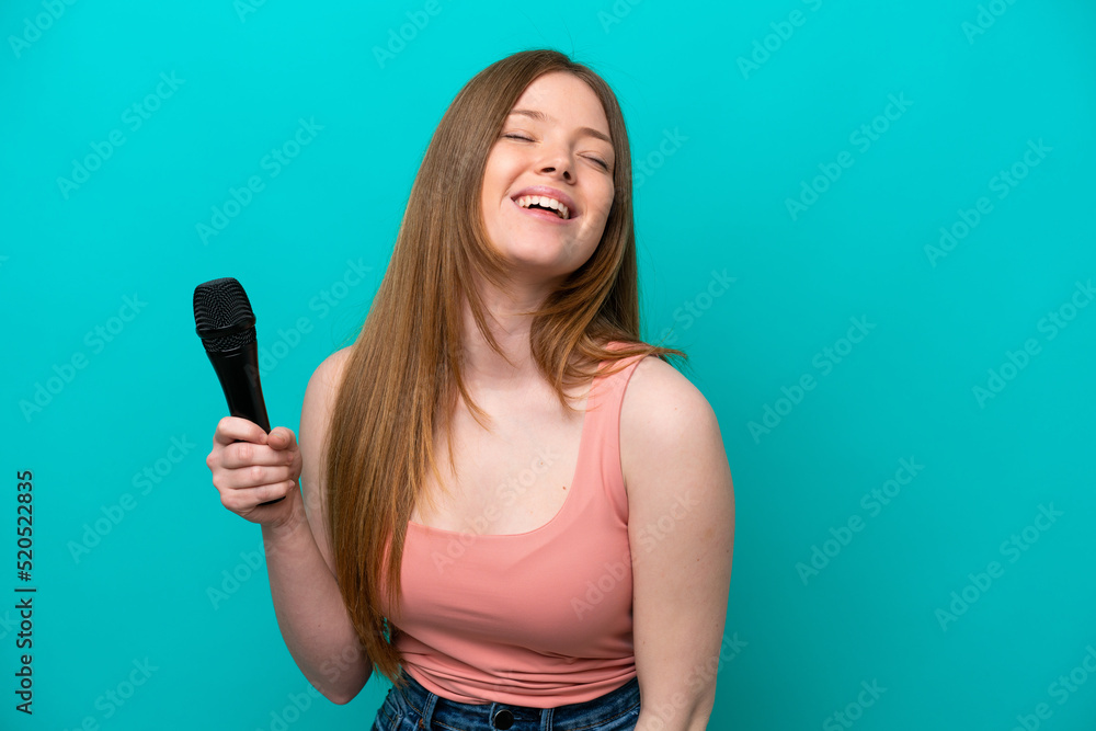 Singer caucasian woman picking up a microphone isolated on blue background laughing Singer caucasian woman picking up a microphone isolated on blue background laughing