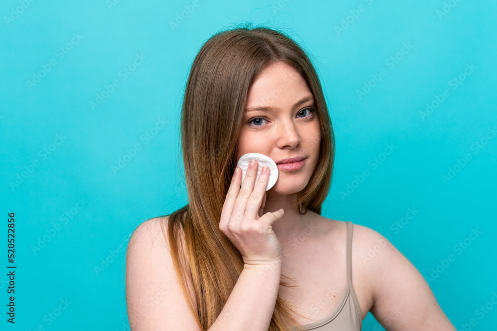 Young caucasian woman isolated on blue background with cotton pad for removing makeup from her face Young caucasian woman isolated on blue background with cotton pad for removing makeup from her face