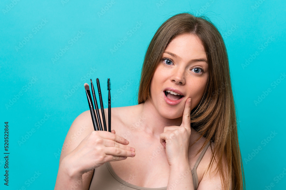 Young caucasian woman isolated on blue background holding makeup brush Young caucasian woman isolated on blue background holding makeup brush