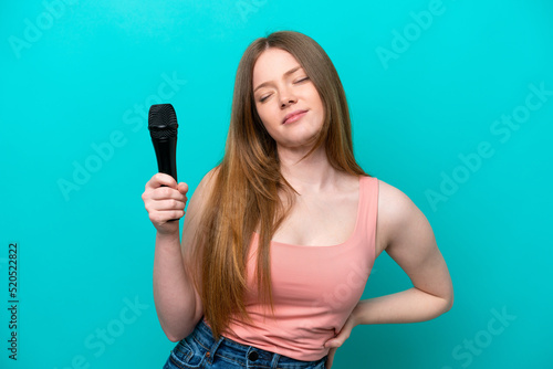 Singer caucasian woman picking up a microphone isolated on blue background suffering from backache for having made an effort