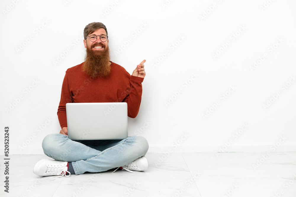 Young reddish caucasian man with laptop isolated on white background pointing finger to the side Young reddish caucasian man with laptop isolated on white background pointing finger to the side