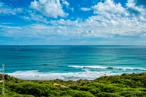 Picturesque ocean landscape with gentle sea waves lapping over quiet beach surrounded by green, beautiful sky with white cloud above. Hokianga, Northland, New Zealand