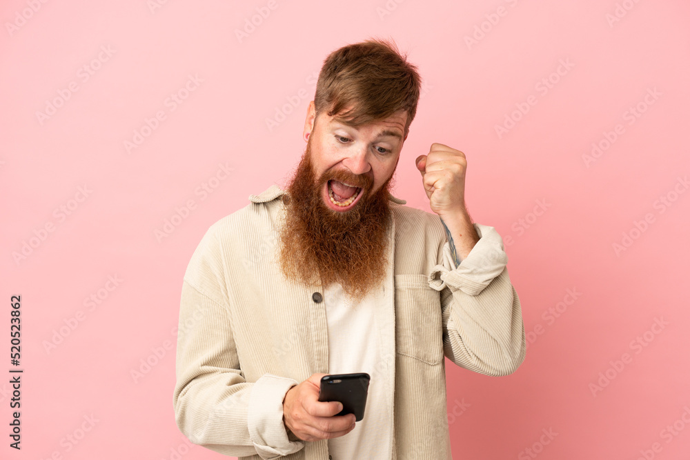 Young reddish caucasian man isolated on pink background surprised and sending a message Young reddish caucasian man isolated on pink background surprised and sending a message