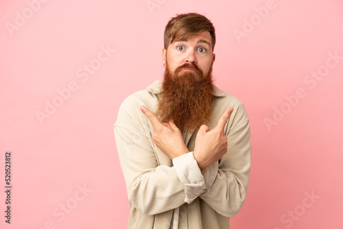 Young reddish caucasian man isolated on pink background pointing to the laterals having doubts © luismolinero