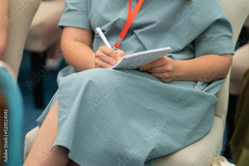 Woman in a mint-colored dress on her knee writes down in a notebook the information she heard at a conference, seminar. Concept of training, professional development