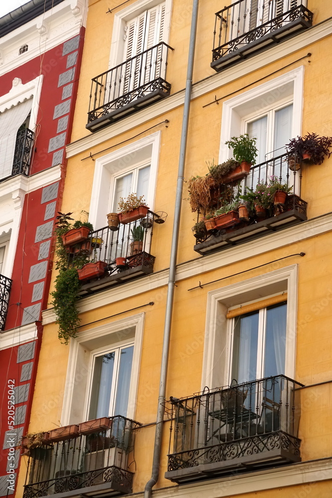 The facade of typical Spanish old house with beautiful balcony with various green plants in summer. Balcony with metal railings.