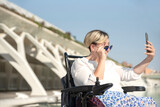 portrait of a smiling disabled woman in a wheelchair taking a selfie looking behind sunglasses