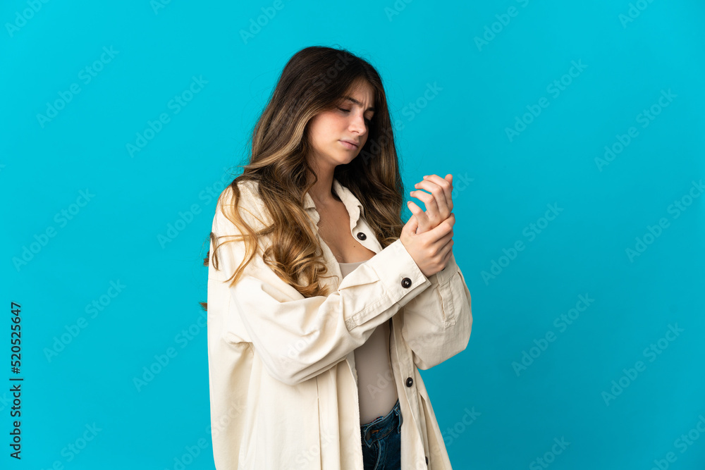 Young caucasian woman isolated on blue background suffering from pain in hands Young caucasian woman isolated on blue background suffering from pain in hands