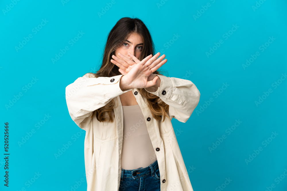 Young caucasian woman isolated on blue background making stop gesture with her hand to stop an act Young caucasian woman isolated on blue background making stop gesture with her hand to stop an act