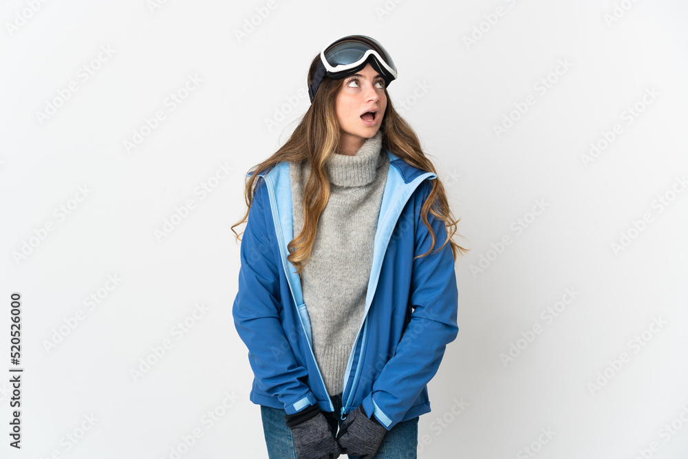 Skier girl with snowboarding glasses isolated on white background looking up and with surprised expression Skier girl with snowboarding glasses isolated on white background looking up and with surprised expression