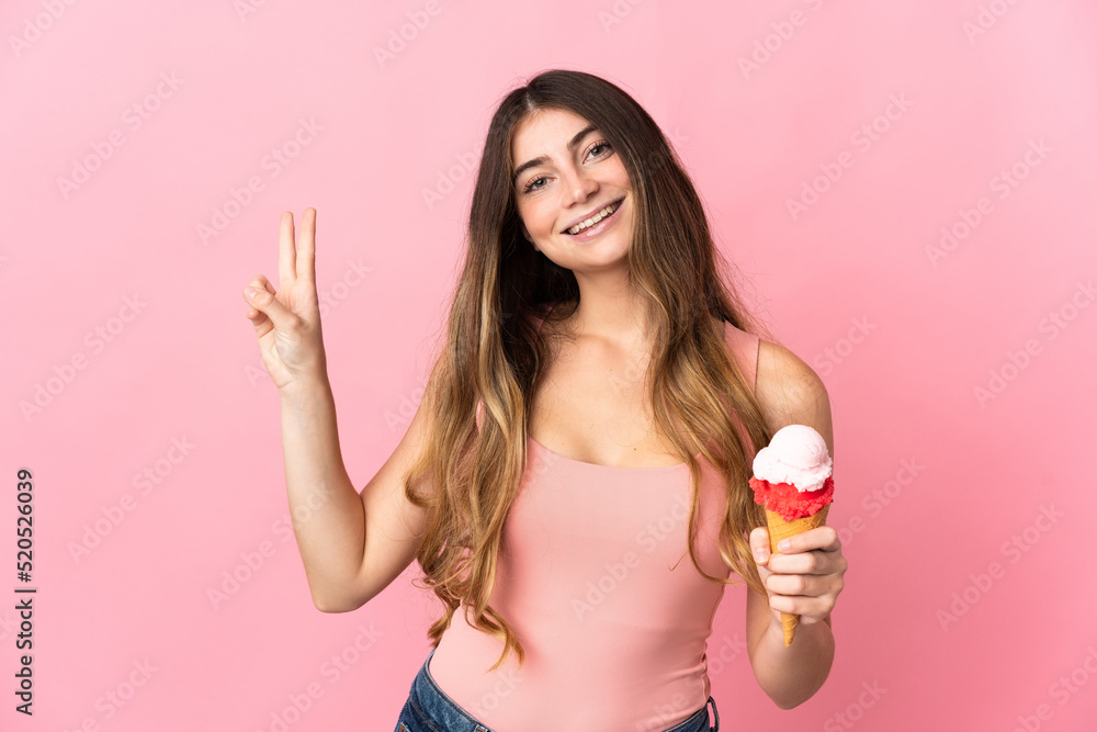 Young caucasian woman with a cornet ice cream isolated on pink background smiling and showing victory sign Young caucasian woman with a cornet ice cream isolated on pink background smiling and showing victory sign