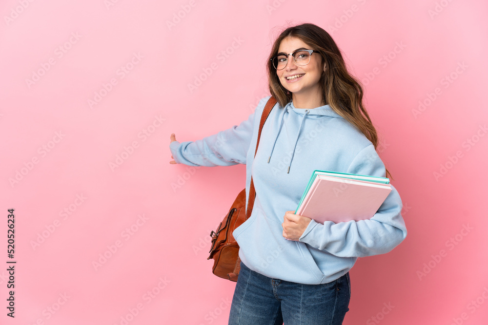 Fototapeta premium Young student woman isolated on pink background extending hands to the side for inviting to come