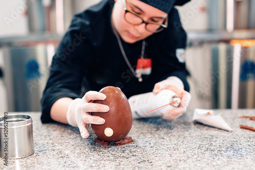 female chocolatier preparing a chocolate egg in her lab kitchen photo