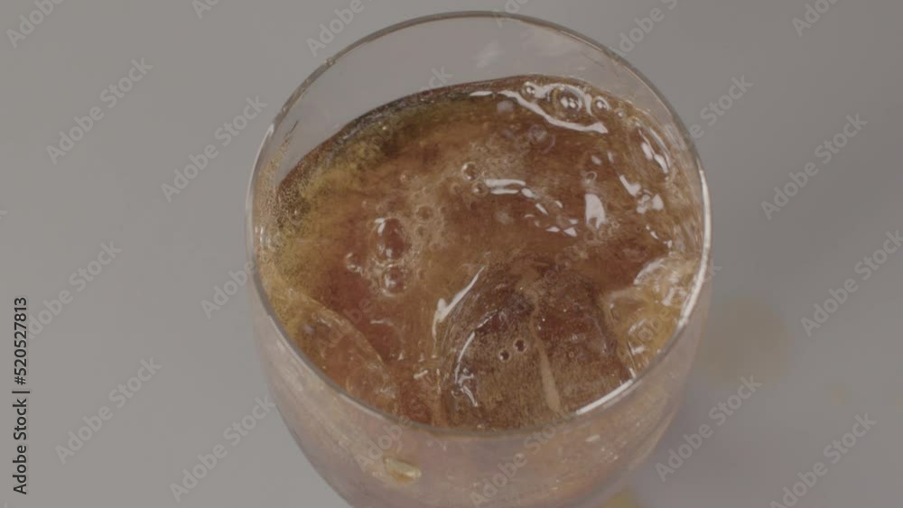 High angle view of Ice cube falling into glass of cola with the liquid splashing in slow motion High angle view of Ice cube falling into glass of cola with the liquid splashing in slow motion